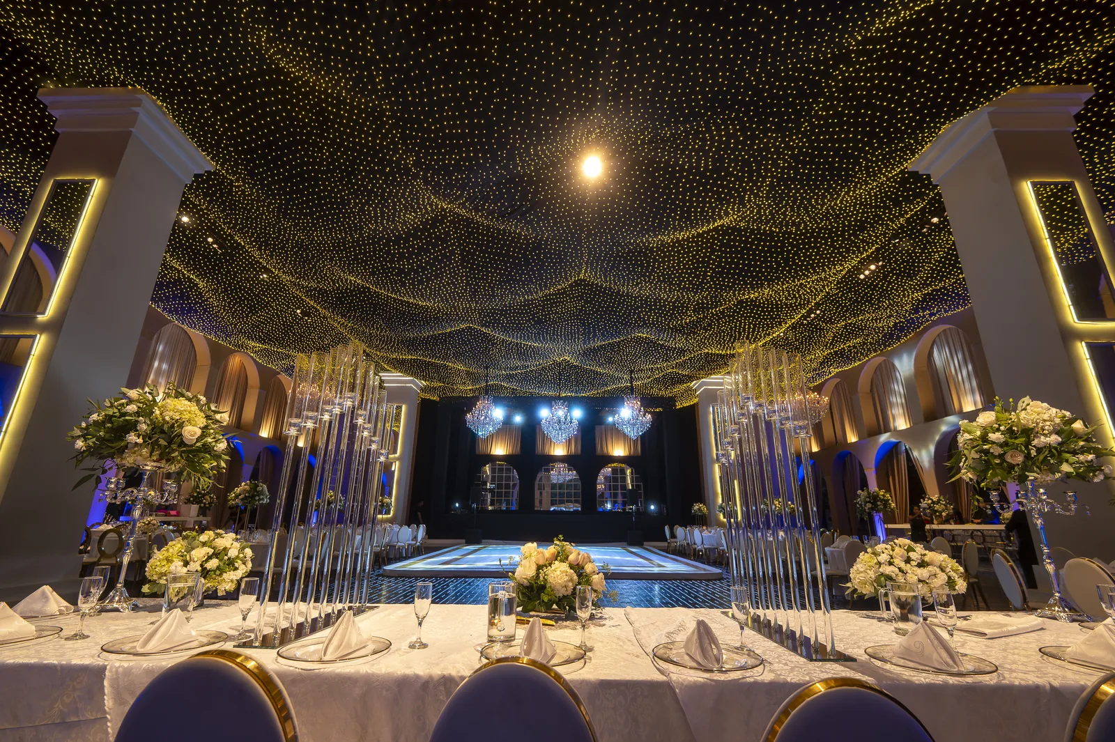 Salón de bodas de lujo MEGA POINT — techo de estrellas doradas y centros de mesa con rosas blancas